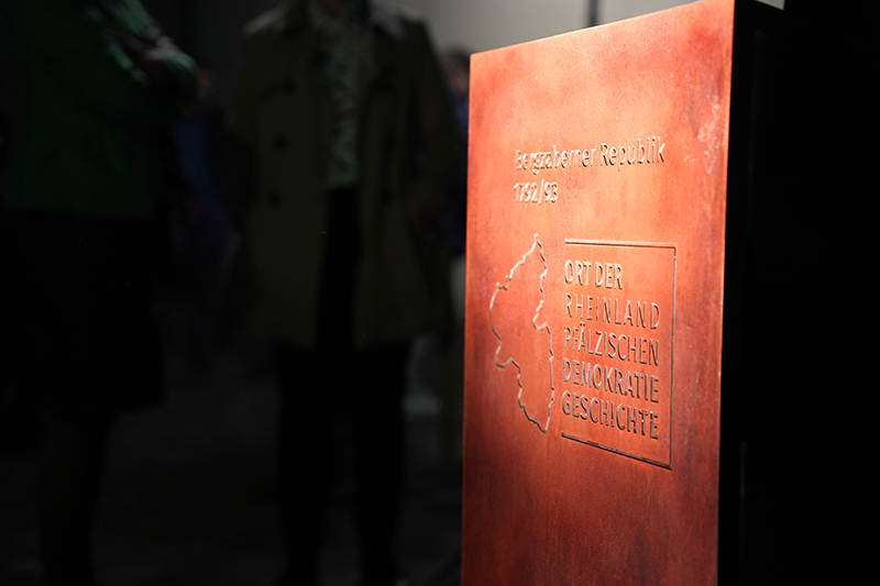 Zu sehen ist ein gro&szlig;er metalliger Gegenstand mit der Aufschrift "Bergzabener Republik 1792/93, Ort der rheinland-pf&auml;lzischen Demokratiegeschichte"